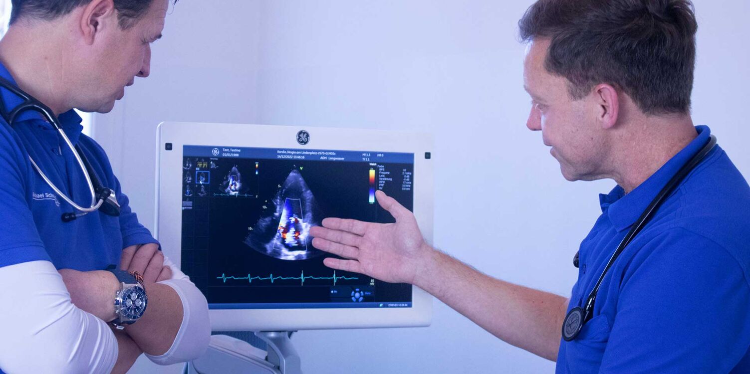 Zwei Ärzte bei einer Untersuchung. Ein Arzt zeigt auf den Bildschirm eines Ultraschallgerätes.