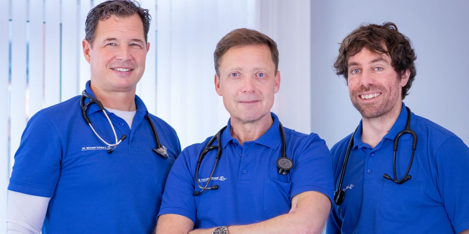 Drei Ärzte stehen nebeneinander. Sie tragen ein königblaues Poloshirt.