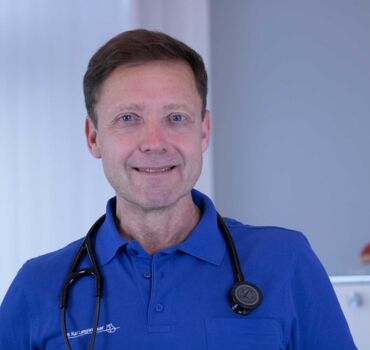 Ein Porträtfoto von Dr. med. Matthias Mohr - Internist | Kardiologe. Er trägt ein blaues Poloshirt und ein Stethoskop um den Hals.